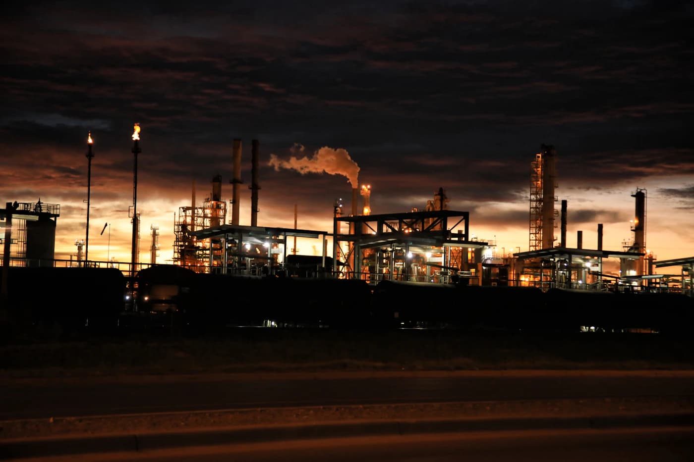 Instalacao industrial iluminada ao entardecer, imagem contextual sobre mercado petrolifero.